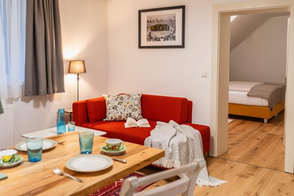 landhaus-apartments-appartement-18-wohnzimmer-sofa-esstisch-gedeckt Wohnzimmer im Apartment #18 mit Sofa, Esstisch und gedecktem Tisch